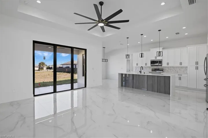 Kitchen featuring white cabinets, a center island with sink, quartz countertops, decorative light features and backsplash, ceramic flooring and ceiling fan