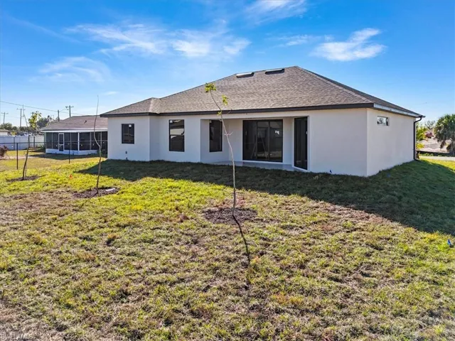 Back of house featuring roof with shingles, stucco siding, a lawn, and a patio