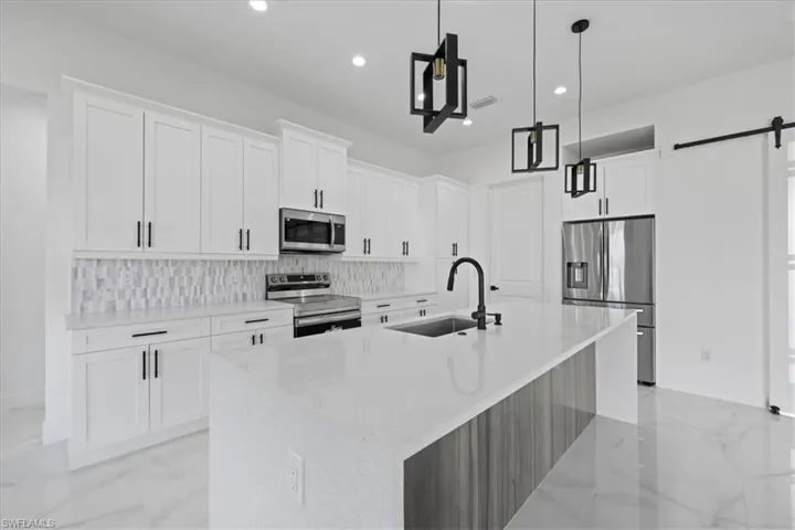 Kitchen featuring stainless steel appliances, pendant lighting, white cabinetry, quartz counters