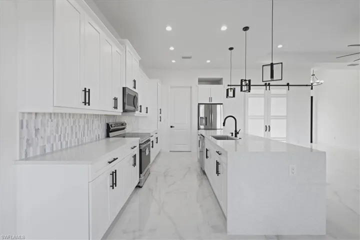 Kitchen with stainless steel appliances, a barn door to Office, quartz counters, white cabinets, and hanging light fixtures
