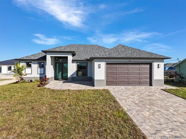 Prairie-style house with stucco siding, a front yard, driveway, an attached garage, and roof with shingles