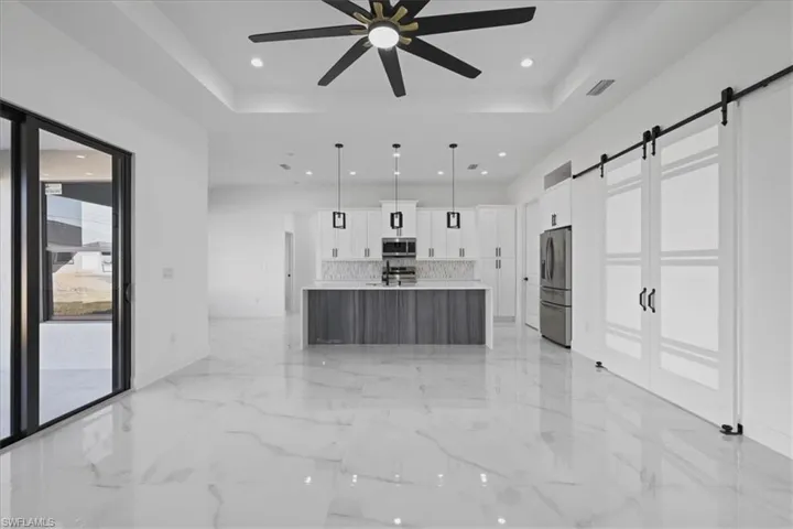 Barn door Office, white cabinets, a center island with sink, hanging light fixtures, and stainless steel appliances