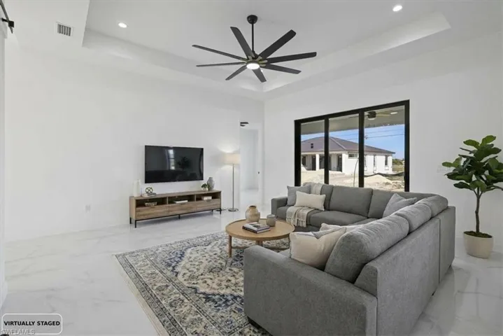 Photo Staged. Living room with a tray ceiling, ceramic floors, a ceiling fan, and recessed lighting
