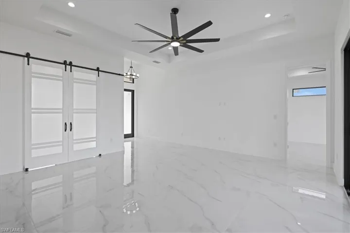 View of entry of primary bedroom and office with barn doors, a raised ceiling, recessed lighting, a ceiling fan, and ceramic finish floors