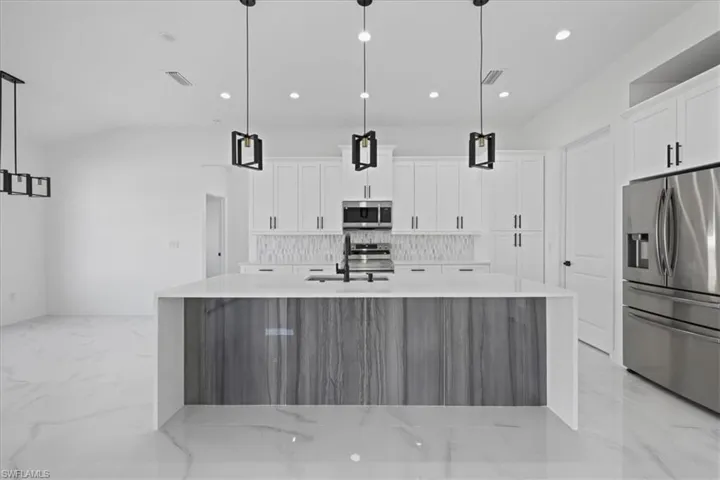 Kitchen with stainless steel appliances, a large island with sink, quartz counters, white cabinets, and recessed lighting