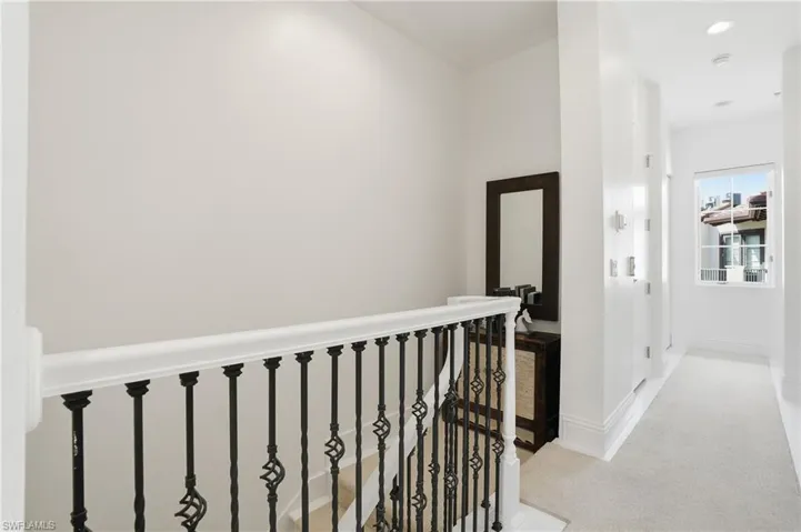 Hallway with light colored carpet and an upstairs landing
