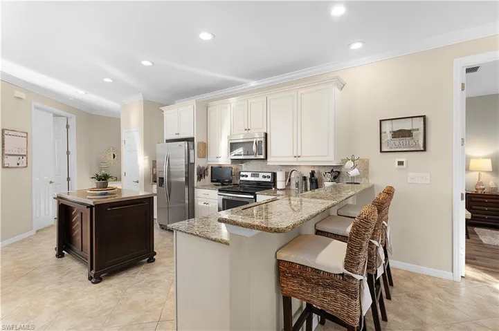 Kitchen featuring stainless steel appliances, light stone counters, kitchen peninsula, decorative backsplash, and a breakfast bar