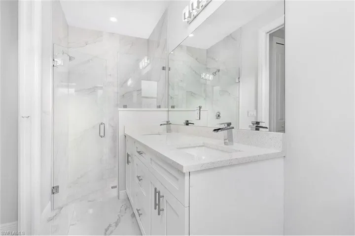 Bathroom with light marble finish floors, double vanity, and a marble finish shower