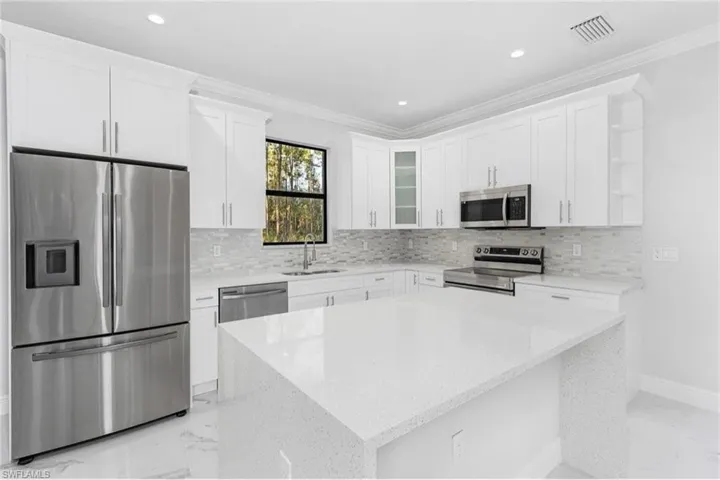 Kitchen with stainless steel appliances, white cabinets, light marble finish flooring, light stone counters, and ornamental molding