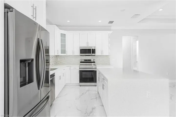 Kitchen with stainless steel appliances, light marble finish floors, white cabinetry, recessed lighting, and ornamental molding