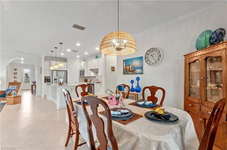 Dining area featuring crown molding, a chandelier, light tile patterned flooring, arched walkways, and recessed lighting
