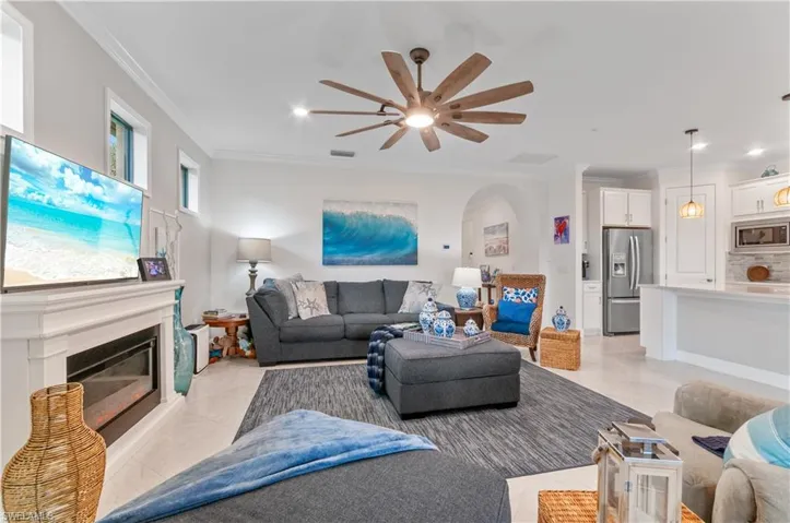 Living area with crown molding, a glass covered fireplace, a ceiling fan, light tile patterned floors, and recessed lighting