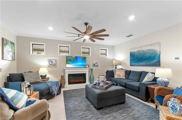 Living room with crown molding, a glass covered fireplace, a ceiling fan, and recessed lighting