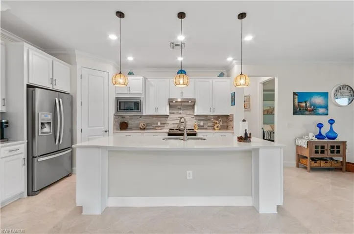Kitchen featuring stainless steel appliances, white cabinetry, crown molding, hanging light fixtures, and a center island with sink
