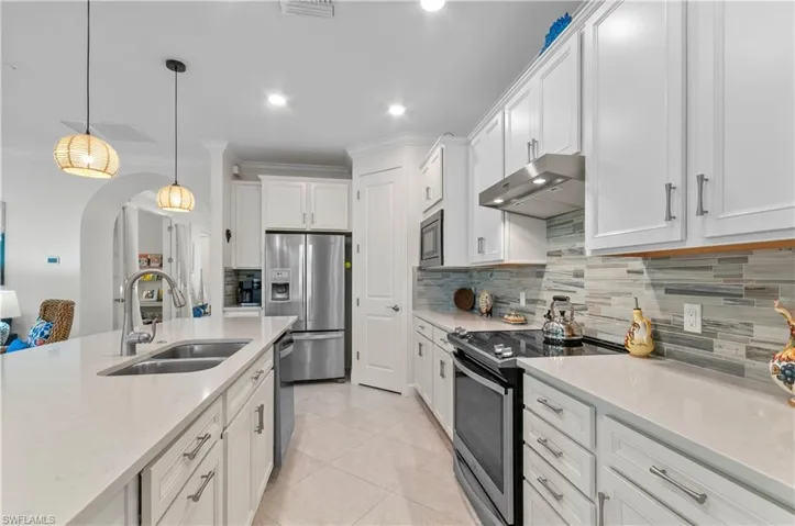 Kitchen featuring appliances with stainless steel finishes, light stone counters, hanging light fixtures, under cabinet range hood, and white cabinets