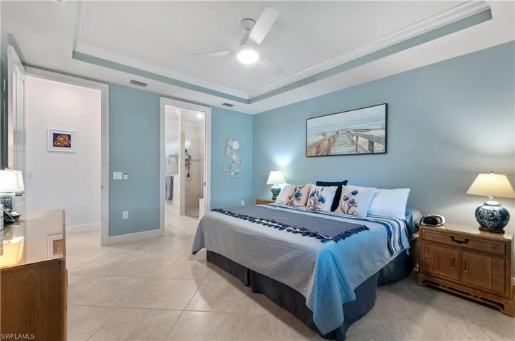 Bedroom featuring a raised ceiling, a ceiling fan, connected bathroom, ornamental molding, and light tile patterned floors