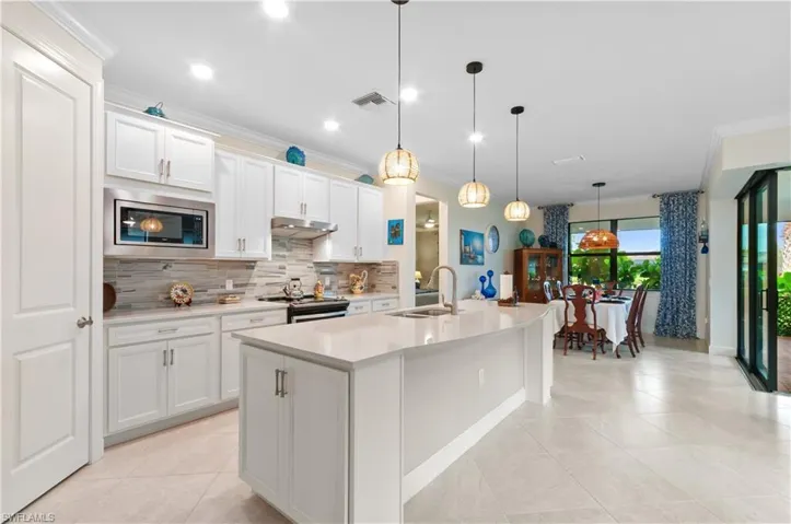 Kitchen with crown molding, hanging light fixtures, a center island with sink, backsplash, and white cabinets