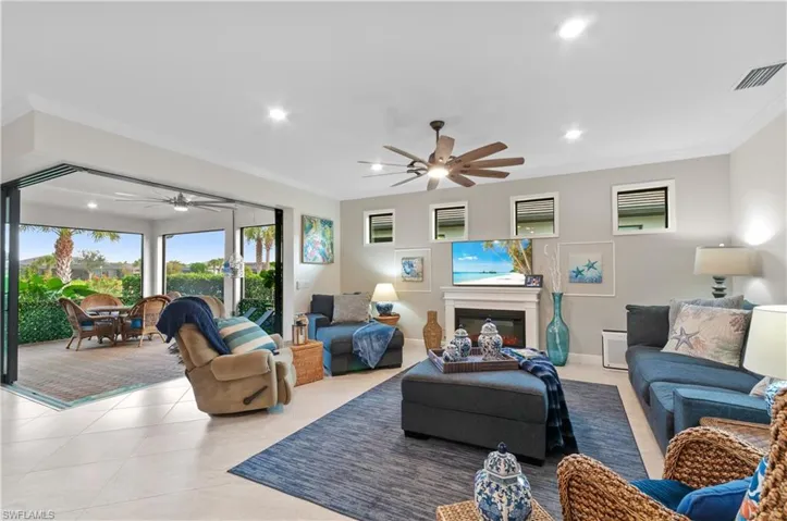 Living room with crown molding, light tile patterned flooring, a ceiling fan, a glass covered fireplace, and recessed lighting