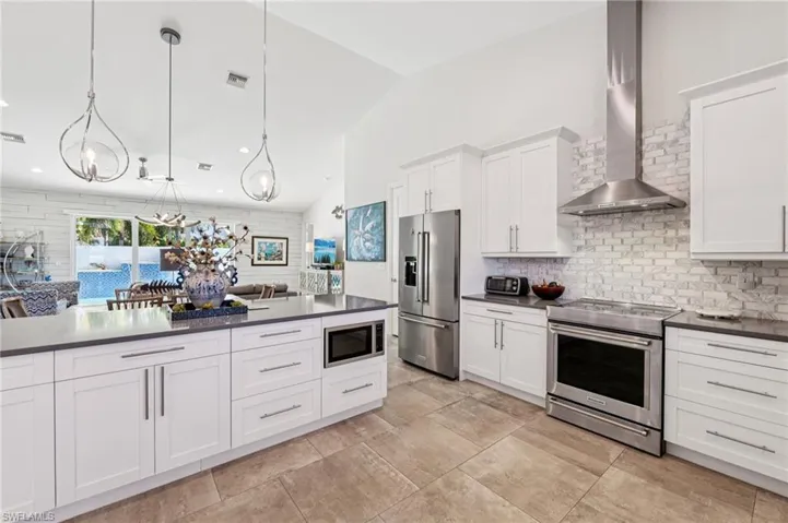 Kitchen featuring high quality appliances, white cabinetry, lofted ceiling, decorative backsplash, and hanging light fixtures