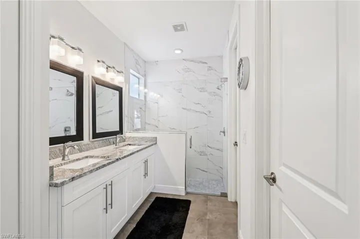Full bath with double vanity and a marble finish shower