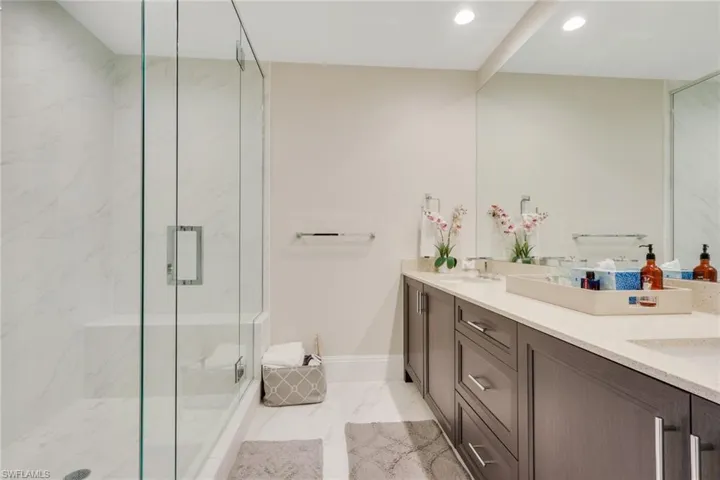 Full bathroom featuring double vanity, a marble finish shower, recessed lighting, and light marble finish floors