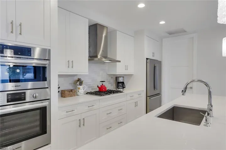 Kitchen featuring stainless steel appliances, white cabinetry, backsplash, recessed lighting, and light stone counters