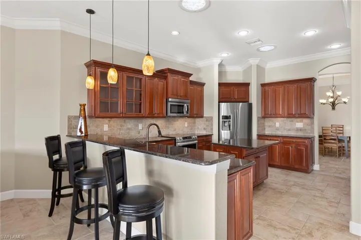 Kitchen featuring kitchen peninsula, tasteful backsplash, stainless steel appliances, dark stone countertops, and hanging light fixtures