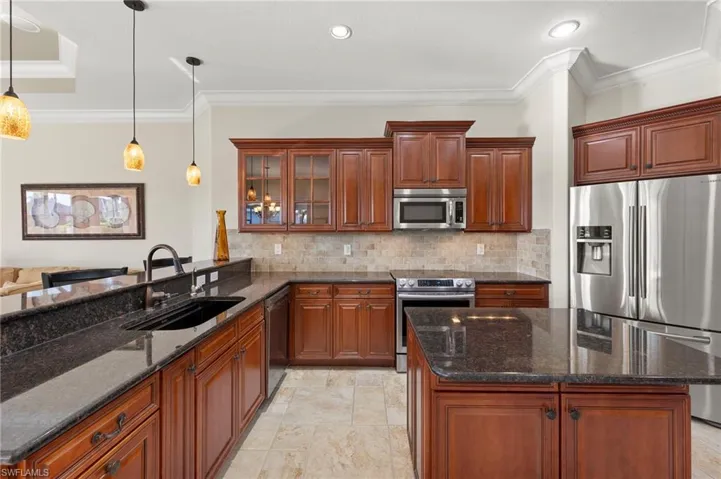 Kitchen with crown molding, hanging light fixtures, dark stone countertops, appliances with stainless steel finishes, and sink