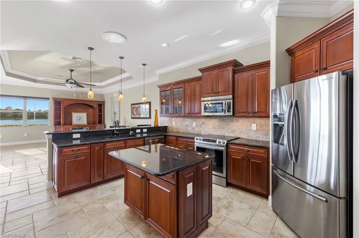 Kitchen with kitchen peninsula, a raised ceiling, ornamental molding, appliances with stainless steel finishes, and pendant lighting