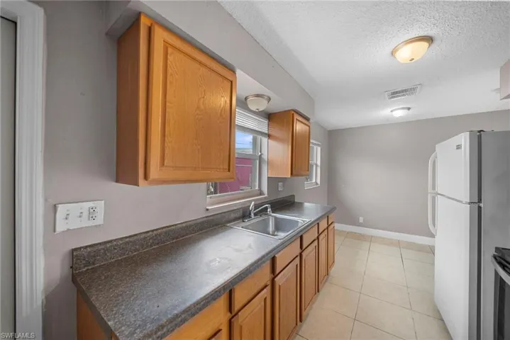 Kitchen featuring wood finish cabinets, dark countertops, a textured ceiling, and light tile patterned floors