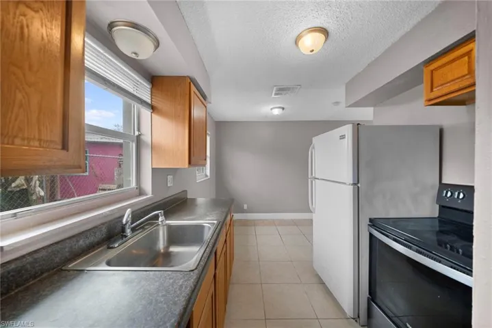 Kitchen featuring wood finish cabinetry, electric range, dark countertops, a textured ceiling, and light tile patterned flooring