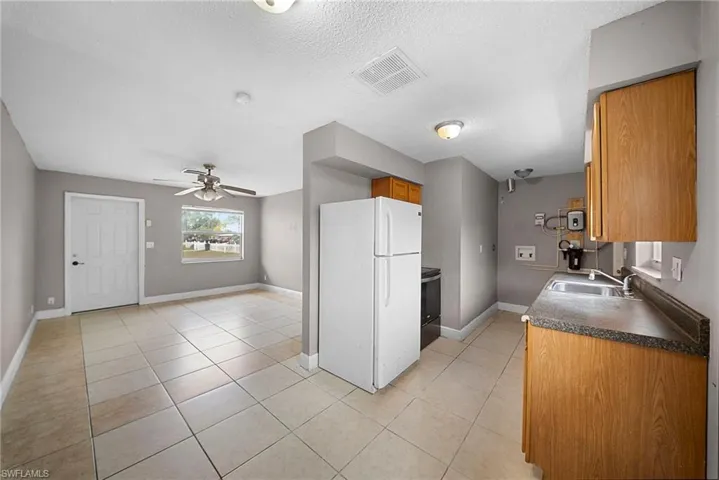 Kitchen featuring freestanding refrigerator, wood finish cabinetry, dark countertops, light tile patterned floors, and ceiling fan