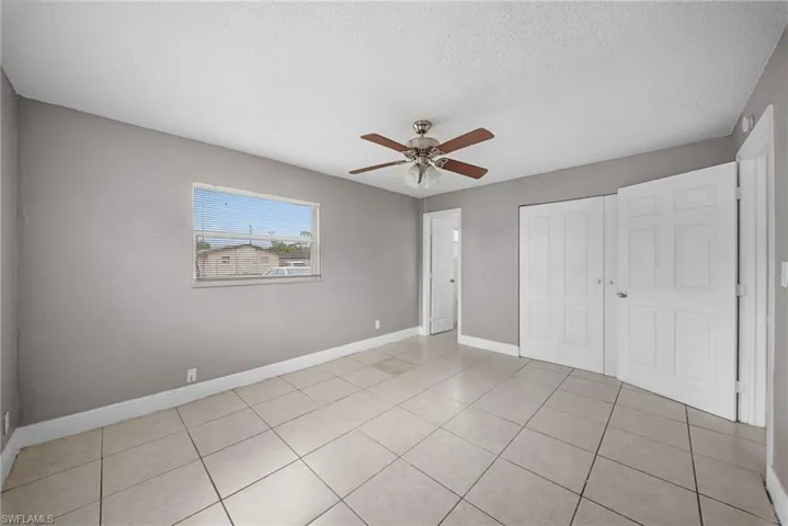 Unfurnished bedroom featuring a closet, a ceiling fan, a textured ceiling, and light tile patterned flooring