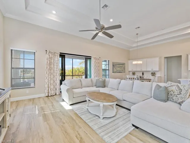Living room featuring ceiling fan with notable chandelier, light hardwood / wood-style tile floors, a towering ceiling, ornamental molding, and a tray ceiling