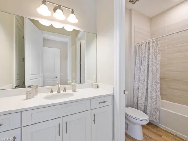 Full bathroom with toilet, vanity, shower / bath combination with curtain, and hardwood / wood-style flooring