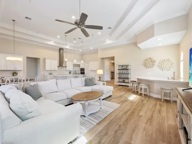 Living room featuring ornamental molding, ceiling fan with notable chandelier, light hardwood / wood-style floors, and a raised ceiling