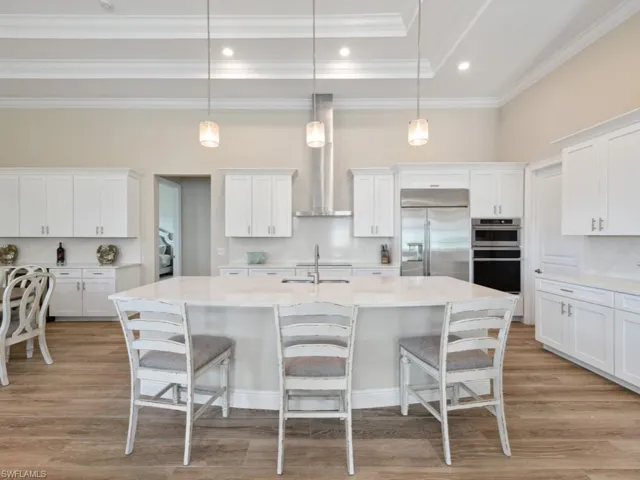 Kitchen with wall chimney exhaust hood, an island with sink, pendant lighting, light wood-type tile flooring, and appliances with stainless steel finishes
