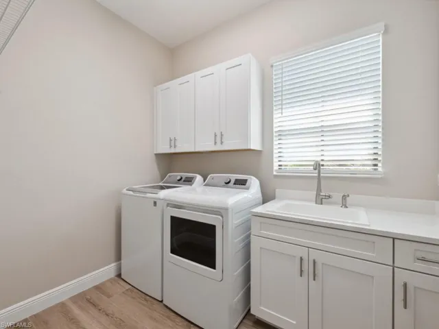 Laundry room featuring cabinets, light wood-type tile flooring, sink, and washing machine and clothes dryer and custom cabinetry.