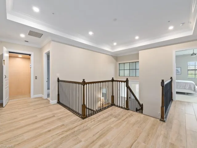 Corridor featuring light wood-style tile floors, a raised ceiling, and crown molding