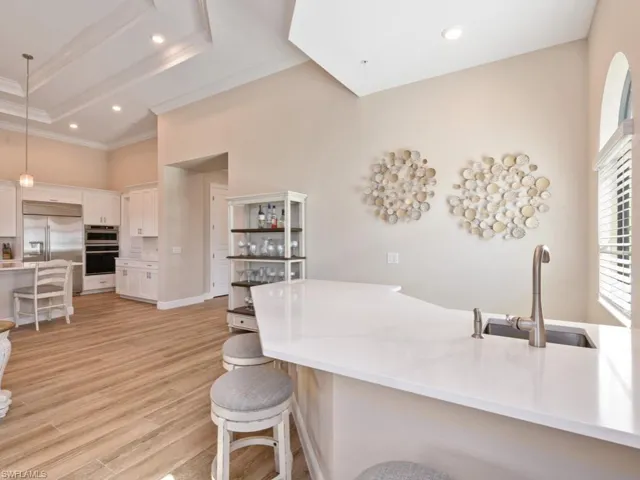 Kitchen featuring stainless steel appliances, wet bar, decorative light fixtures, light wood-style tile flooring, and white custom cabinets.