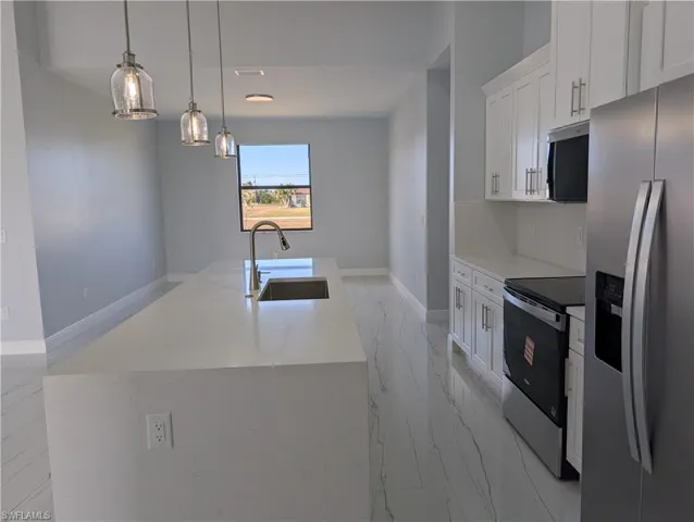 Kitchen featuring stainless steel appliances, light marble finish floors, white cabinetry, pendant lighting, and light stone counters