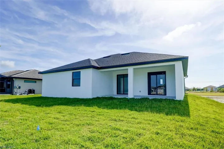 Rear view of house with stucco siding, a lawn, and a patio