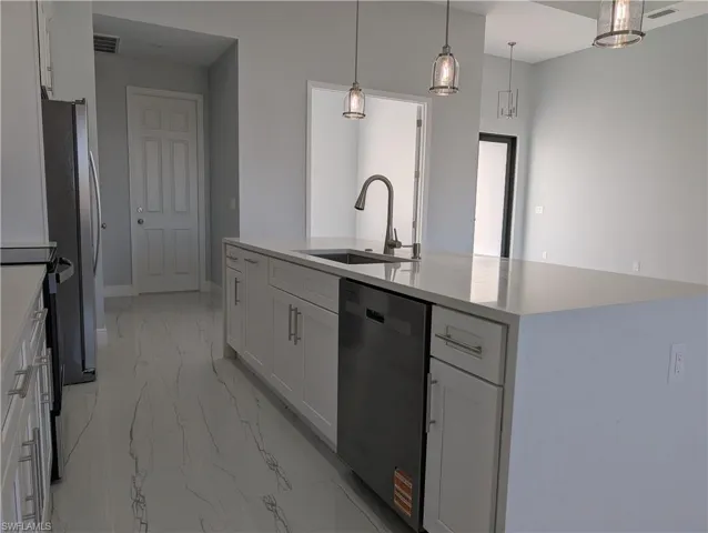 Kitchen featuring white cabinetry, appliances with stainless steel finishes, pendant lighting, and light stone countertops