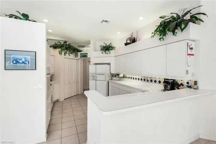 Kitchen with a peninsula, light countertops, white refrigerator with ice dispenser, white cabinets, and backsplash