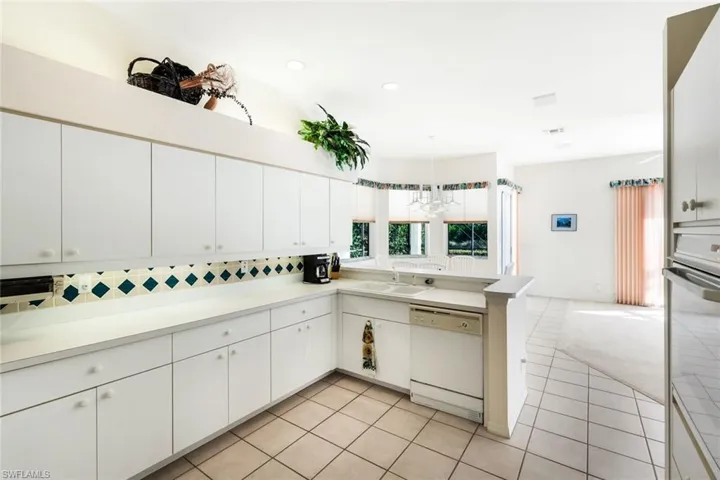 Kitchen featuring a peninsula, dishwasher, light countertops, oven, and white cabinetry