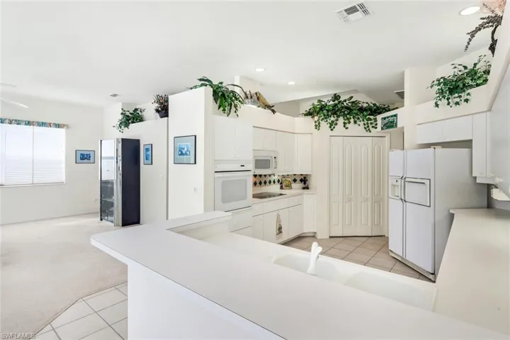 Kitchen featuring white cabinetry, light carpet, light countertops, light tile patterned floors, and white appliances