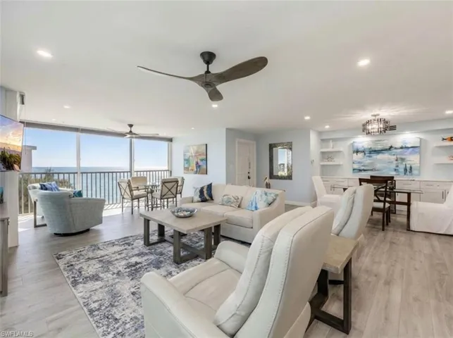 Living area featuring light wood-style flooring, floor to ceiling windows, hanging lights, a ceiling fan, and a water view