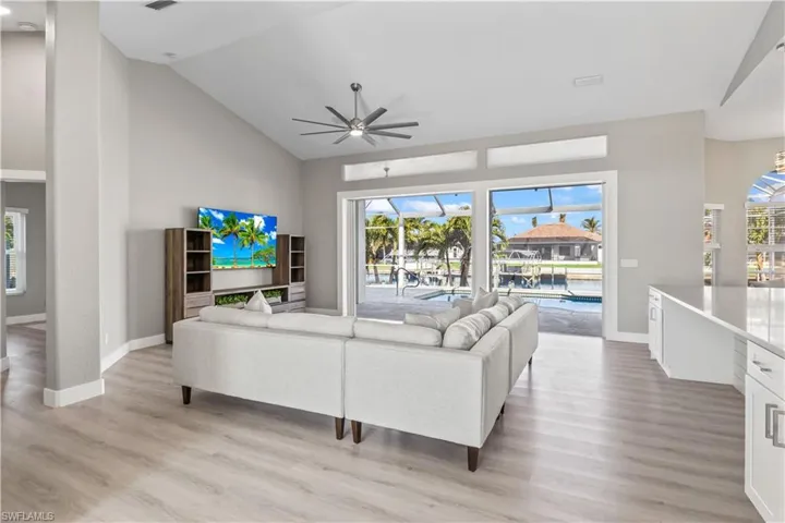 Living area with a sunroom, plenty of natural light, light wood finished floors, and high vaulted ceiling