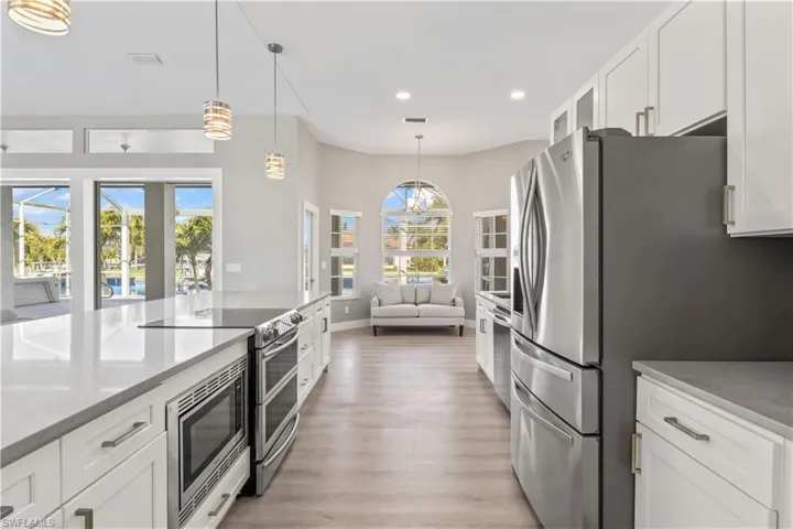 Kitchen featuring white cabinetry, stainless steel appliances, open floor plan, hanging light fixtures, and light wood-style flooring