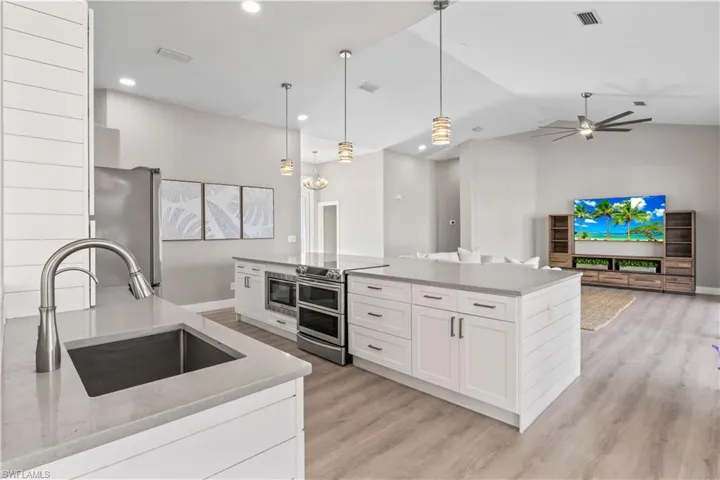 Kitchen with decorative light fixtures, white cabinets, appliances with stainless steel finishes, open floor plan, and light stone countertops